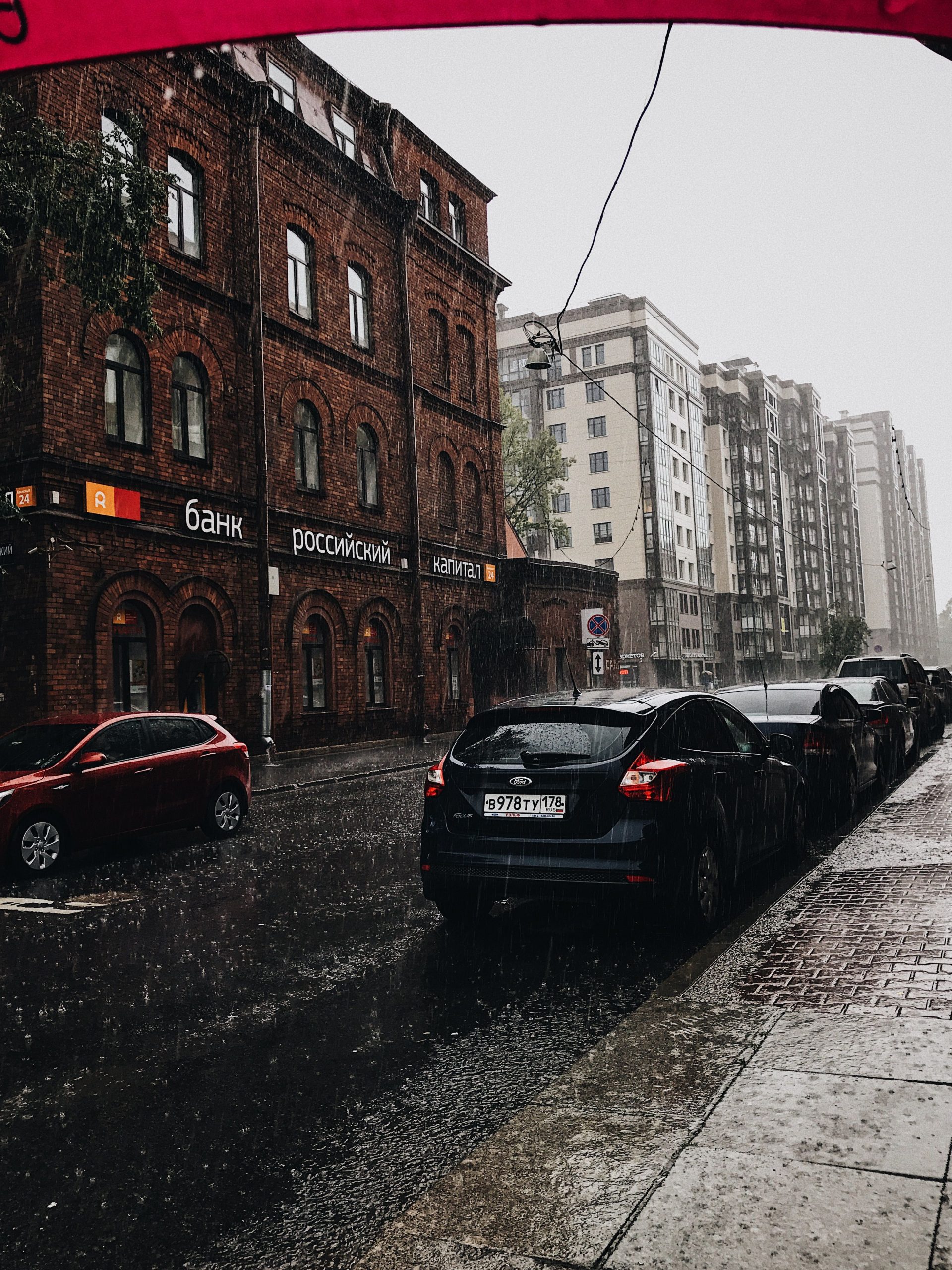A rainy urban scene with wet streets and parked cars in Saint Petersburg, Russia, capturing the city's architecture.